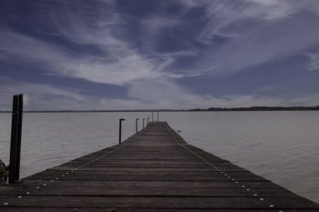 a wooden platform or jetty over the water in a lake with a blue sky with white clouds. wooden jetty in the chiemsee in germany