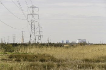 Line of electric pylons into distance above countryside, Hinkley Point Nuclear Power Station in distance, landscape