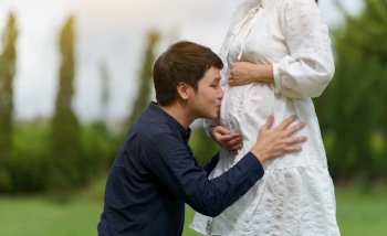 married couple is expecting a baby. man kissing belly of his pregnant wife in the park