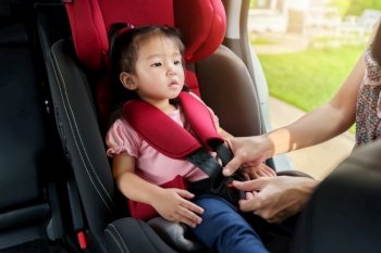 mother is fastening safety belt to toddler girl in car seat before go for ride
