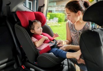 happy mother is fastening safety belt to toddler girl in car seat before go for ride