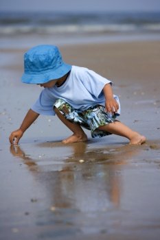  Little boy standing with his feet in the sea looking for shells 