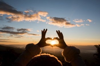 Silhouette hands forming a heart shape with sunrise