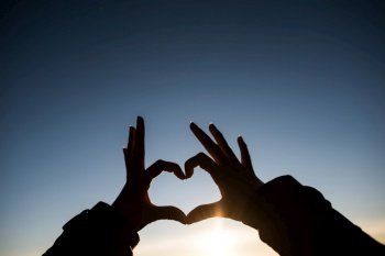 Silhouette hands forming a heart shape with sunrise
