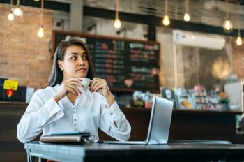 woman sitting happily drinking coffee in cafe shop and labtop