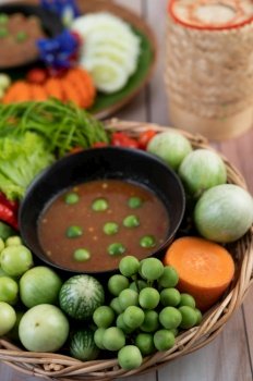 Chili paste paste in a bowl with eggplant, carrots, chili, cucumbers in a basket on wood table