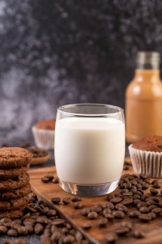 Milk in a glass, complete with coffee beans, cupcakes, bananas and cookies on a wooden plate.