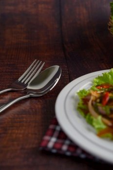 Vertical image and Selective focus sparken stainless fork and spoon, blurred spicy salad of sardine in tomato sauce mixed with herb in white plate on wooden table, copy space