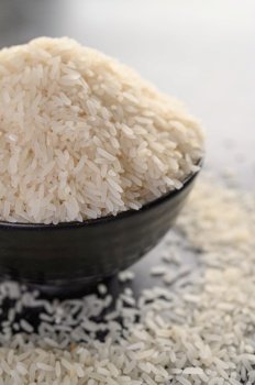 Milled rice in a black bowl on the black cement floor. Selective focus