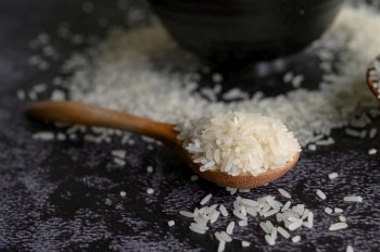 Milled rice in a bowl and a wooden spoon on the black cement floor. Selective focus