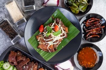 Fried pork topped with sesame seeds along with tomatoes Cabbage and mint, put on a banana leaf in a black dish.