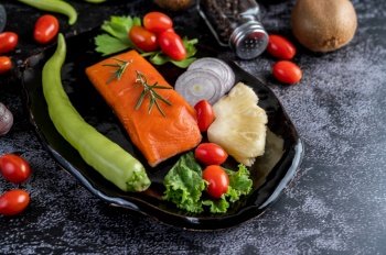 Raw salmon fillets, pepper, kiwi, pineapples, and rosemary onto a plate and black cement floor.