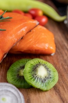 Raw salmon fillets, pepper, kiwi, pineapple and rosemary, wood chopping boards and black cement floors.Selective focus kiwi.
