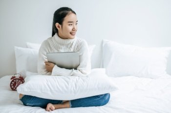 A woman sitting on the bed, hugging the laptop and smiling.