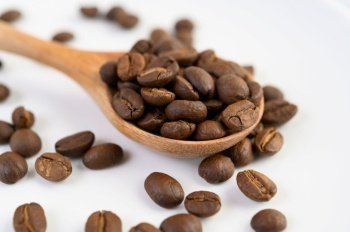 Coffee beans on wooden spoon on a white wood table.