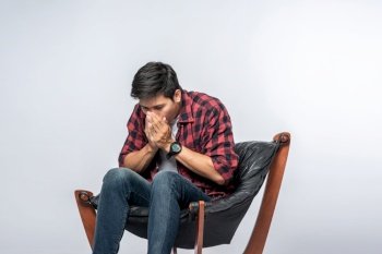 The man in a striped shirt sits sick and sits on a chair and crosses his arms.