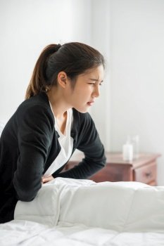 A woman sitting in bed with abdominal pain and pressing her hand on her stomach.