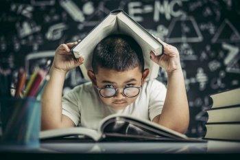 A boy with glasses studied and put a book on his head in the classroom.