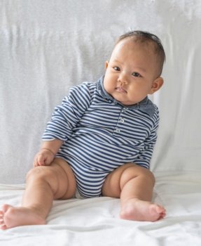 A baby learns to sit on a white bed