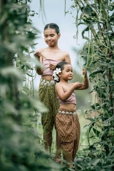 Portrait of lovely girls in Thai traditional dress and put white flower on her ear, standing in plant yard of long beans, They are smile with happiness