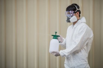 Portrait Disinfection specialist man in PPE suit, gloves, mask and face shield performing public decontamination, standing and holding bottle for spray disinfectant to remove covid-19  