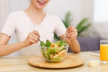 Lifestyle in living room concept, Young Asian woman mixing vegetable salad in bowl for breakfast.