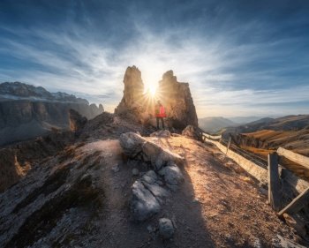 Woman on the mountain trail and stones at sunset in autumn in Dolomites, Italy. Sporty girl on the path and high rocks in fall. Colorful landscape with cliffs, stones, blue sky. Trekking and hiking. Woman on the mountain trail and stones at sunset in autumn