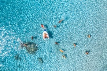 Aerial view of happy people swimming in blue sea at sunset in summer. Vacation in Sardinia, Italy. Top down view of clear azure water, sandy beach, boat. Colorful tropical landscape. Travel. Concept
