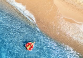 Aerial view of a young woman swimming with red swim ring in blue sea with waves at sunset in summer. Tropical landscape with girl, clear water, sandy beach. Top view. Vacation. Sardinia island, Italy	