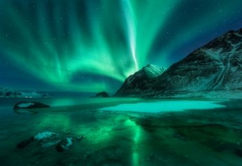 Northern lights above Vik beach at night in Lofoten islands, Norway. Beautiful aurora borealis in winter. Starry sky with polar lights. Landscape with aurora, sea coast, stones, snowy mountains. Space