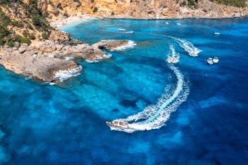 Aerial view of speed boats and yachts in transparent blue water, rocky sea coast, beach at sunny day in summer. Travel in Sardinia, Italy. Top view from drone of sea bay, motorboats, mountain. Travel