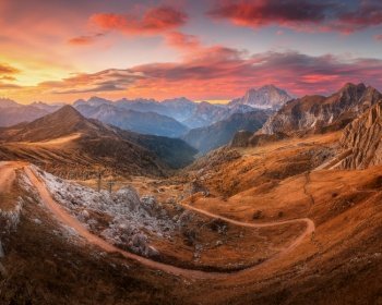 Beautiful mountains and red sky at sunset in autumn. Nature in Dolomites, Italy. Colorful panoramic landscape with rocks, orange grass in hills, trail, dirt road, stones, sky with clouds in fall