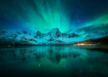 Northern lights over the snowy mountains, frozen sea, reflection in water at night in Lofoten, Norway. Aurora borealis and snow covered rocks. Winter landscape with polar lights, starry sky and fjord