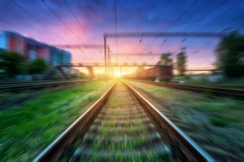 Railroad with motion blur effect at sunset in summer. Industrial landscape with railway station and blurred background with colorful sky, green grass. Railway platform in speed motion. Concept