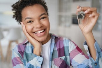 Joyful biracial teen girl tenant showing keys to first new home. Happy mixed race young lady holds apartment key delighted with buying or renting housing. Separation from parents concept.. Happy biracial teen girl tenant showing keys to first new home. Separation from parents concept