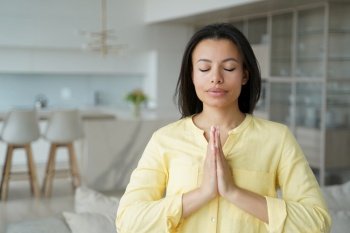 Calm female meditating standing at home with eyes closed put hands together in prayer, mindful woman makes namaste yoga gesture to keep calmness. Healthy lifestyle, meditation, stress relief concept.. Female makes namaste yoga gesture, keeping calmness, praying at home. Meditation, stress relief