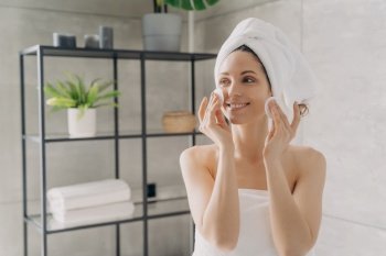 Pretty hispanic girl cleansing facial skin by cotton pads. Smiling female wrapped in towels wipes off makeup after the shower in bathroom. Skincare daily routine, natural woman beauty concept.. Hispanic girl cleanse skin by cotton pads after shower in bathroom. Skincare routine, natural beauty
