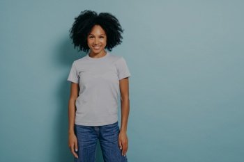 Delighted young african female isolated over blue background with pleasant smile, wearing casual white tshirt and jeans, being in good mood and demonstrating positiveness. Happy mixed race woman. Delighted young african female posing isolated over blue background with pleasant smile