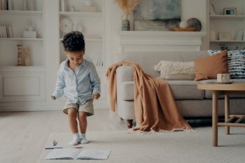 Happy mixed race little boy enjoying playing alone, drawing with pencils on warm carpeted floor, cute smiling african american kid having fun at home. Creative children activity indoor concept. Happy mixed race little boy enjoying playing alone at home, having fun in living room