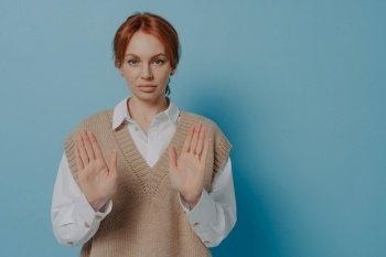 Dont bother me, please. Displeased young 30s red haired woman showing no gesture and demonstrating disagreement, rejecting offer while standing isolated on blue wall background. Displeased young 30s red haired woman showing NO gesture, isolated on blue background