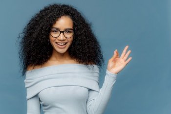 Brilliant idea! Pleased dark skinned young female makes okay gesture, smiles broadly, approves somebodys suggestion, dressed in blue jumper, isolated on blue background. Body language concept
