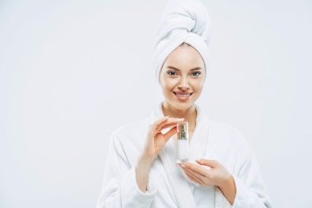 Beautiful spa young woman with healthy fresh skin applies anti aging lotion or cosmetic cream, uses day moisturizer, stands indoor, dressed in bath robe and towel, takes shower before going out