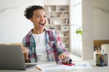Excited happy overjoyed mixed race high school girl student celebrating victory, got entrance letter, email with great exam test scores, good news, screaming yes, sitting at laptop computer at home.. Excited happy mixed race high school girl student celebrating personal achievement sitting at laptop