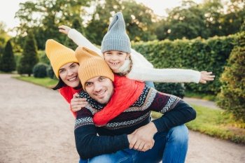Handsome young man spends his free time with family, recieves embrace from adorable daughter and pretty wife, have picnic during autumn weekend. Happy affectionate family have good relationships.