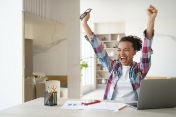 Excited happy african american girl student got good exam test scores on laptop. Overjoyed teenage schoolgirl raising hands screaming celebrates personal achievement or finishing homework.. Overjoyed african american student teen girl got email with good exam scores, celebrates success