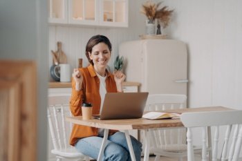 Business lady has online conference. Confident young woman wins. Girl is working in front of computer. European woman is happy. Distance work at the kitchen on quarantine concept.. Business lady has online conference. Confident woman wins. Distance work at kitchen on quarantine.
