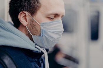 Close up shot of serious man walks in crowded places, commutes to work in underground, wears medical mask for face protection during outbreak and coronavirus infection. Disease protection concept