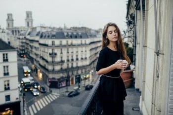 Sensual pretty woman with eyes closed standing on balcony with cup in Paris, France.. Sensual woman on balcony
