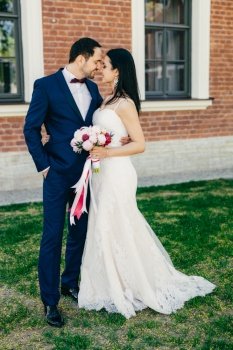 Affectionate wedding young couple going to kiss, being happy to celebrate their wedding. Lovely brunette female in white dress and handsome bridegroom in black fashionable suit. Togetherness concept