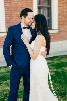 People, relationship and marriage concept. Just married bride and bridegroom kiss passionately, express real emotions, love and feelings. Gorgeous married couple pose outdoor on green grass.